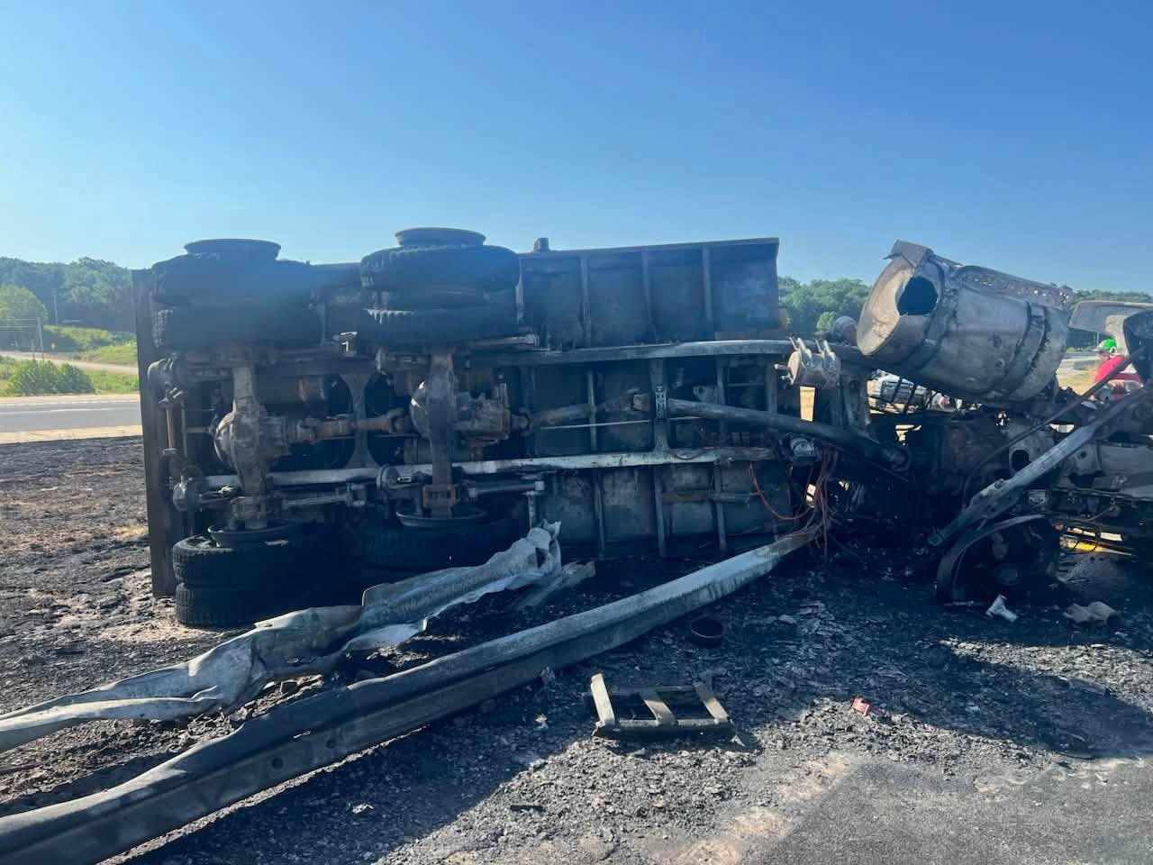 Overturned burned dump truck on the roadside before recovery