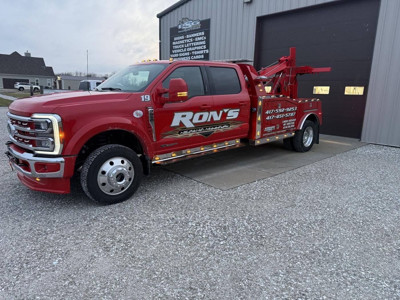 Red Ron's Ford F-550 wrecker with gold lettering, parked by a garage door