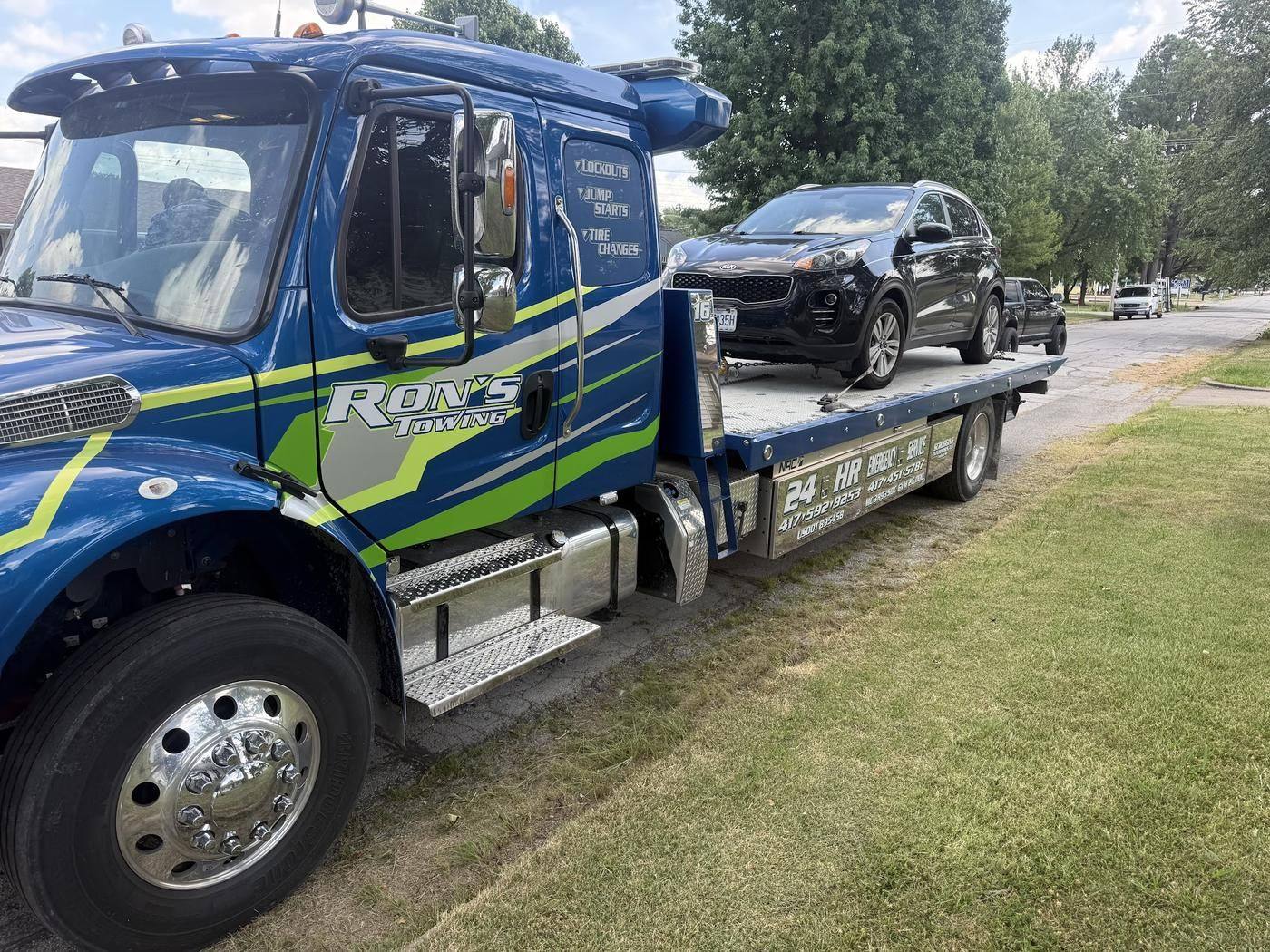 Blue Ron's Towing flatbed carrying an SUV, door lettered lockouts, jump starts, tire changes